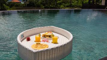 Montaje de comedor flotante con comida y bebidas en una piscina transparente.