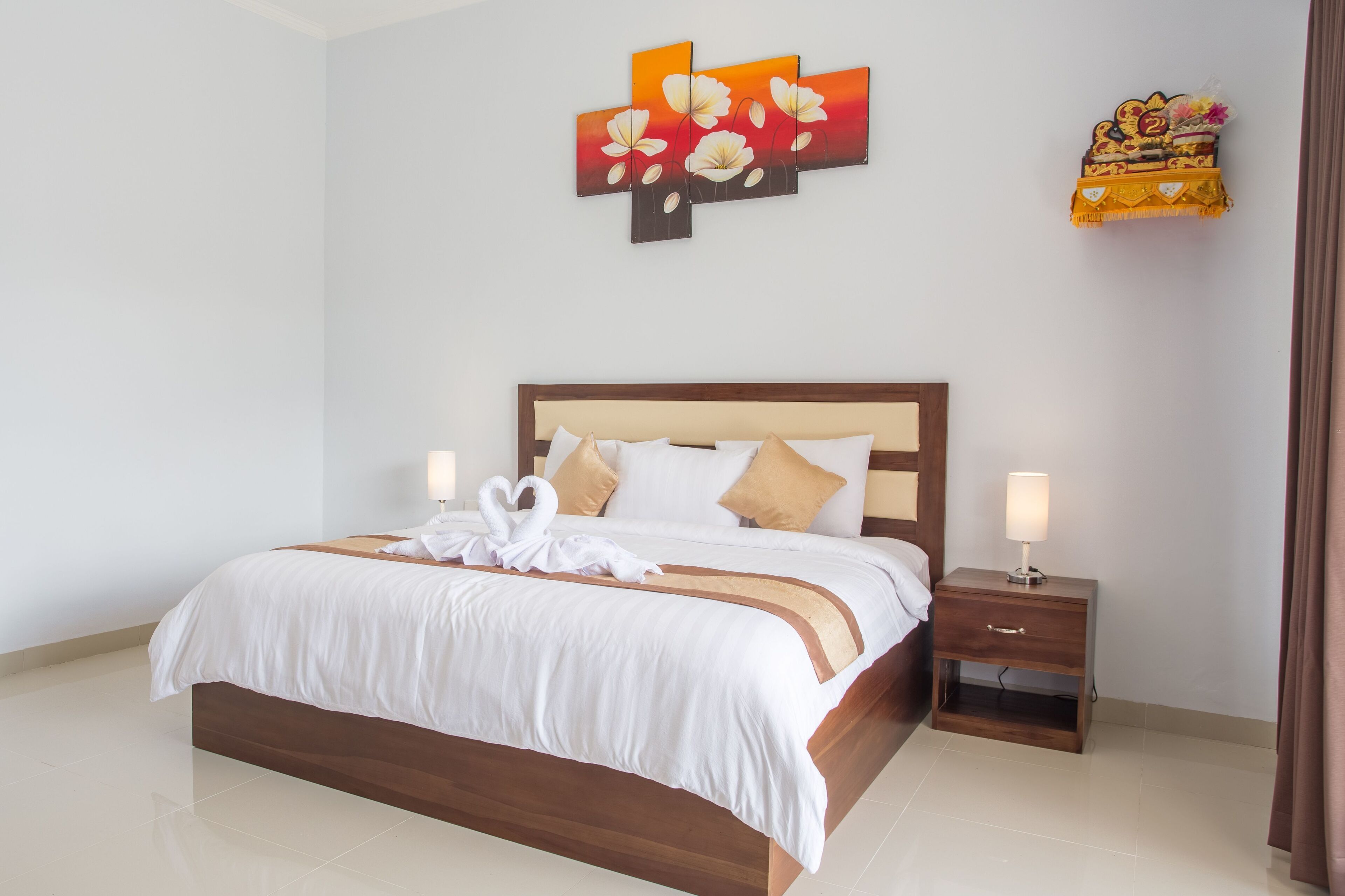 A neatly made bed with white linens and two pillows, a bedside table with a lamp, and a wall art piece above the bed.