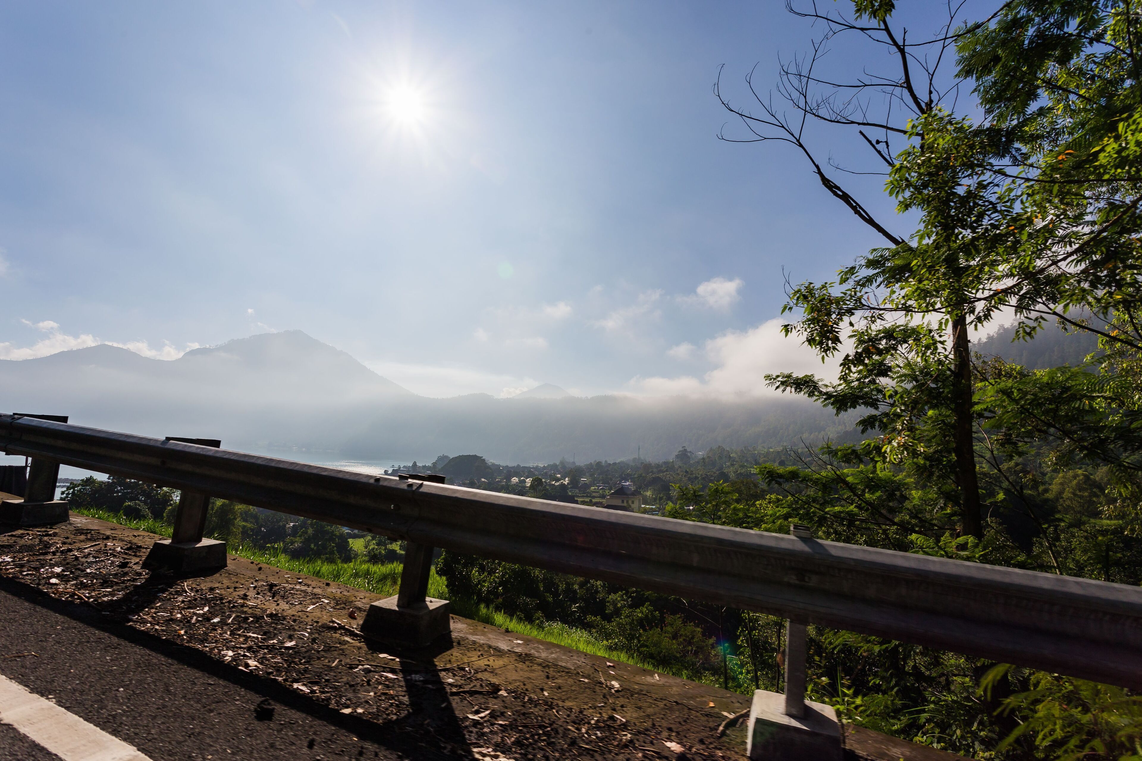 A road with a guardrail, a mountain in the background, and a clear sky.