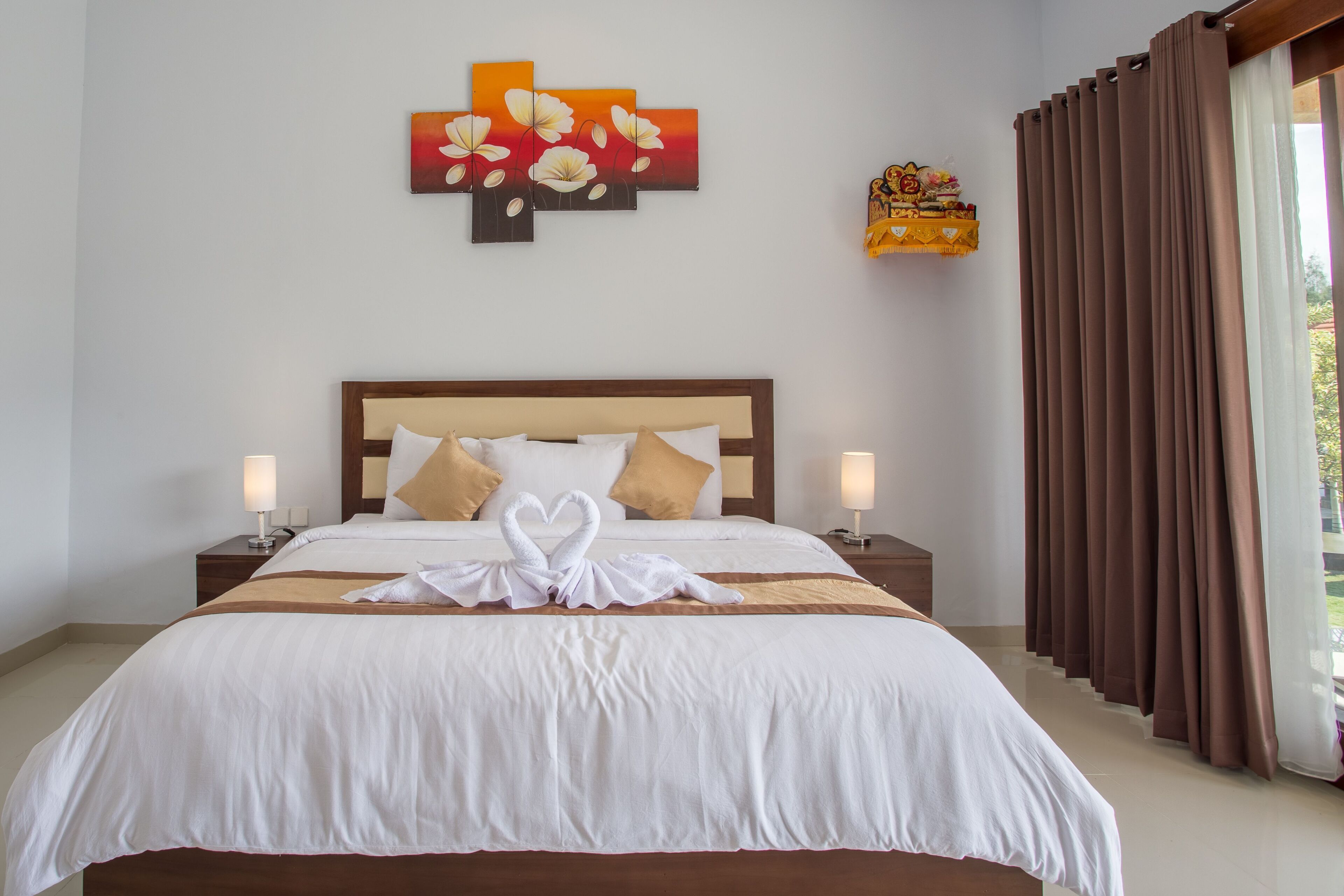 Una cama bien hecha con sábanas blancas y dos almohadas, una obra de arte en la pared encima y una ventana con cortinas marrones.