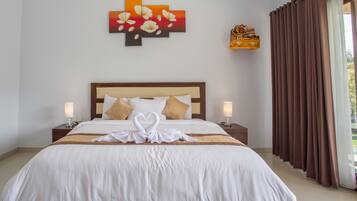 Una cama bien hecha con sábanas blancas y dos almohadas, una obra de arte en la pared encima y una ventana con cortinas marrones.