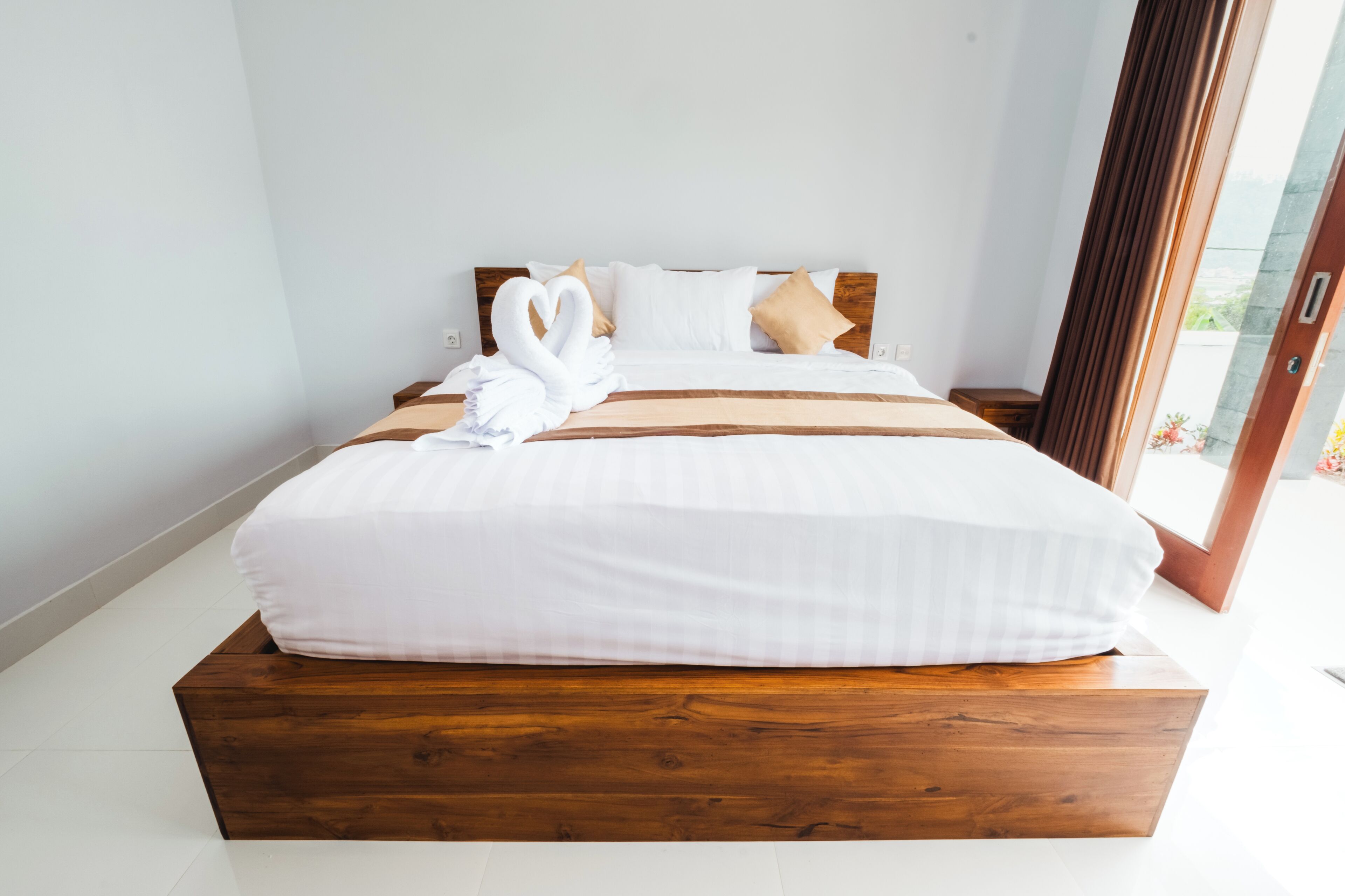 Een groot bed met een houten platform, witte beddengoed en twee zwaanvormige kussens.