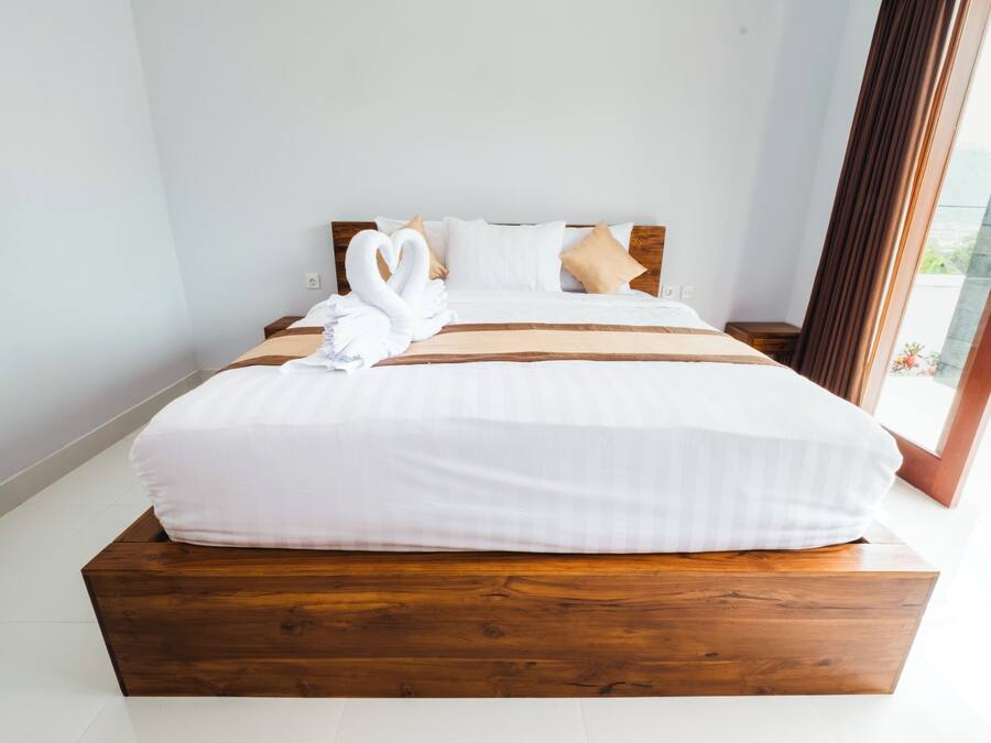 A large bed with a wooden platform, white bedding, and two swan-shaped pillows.