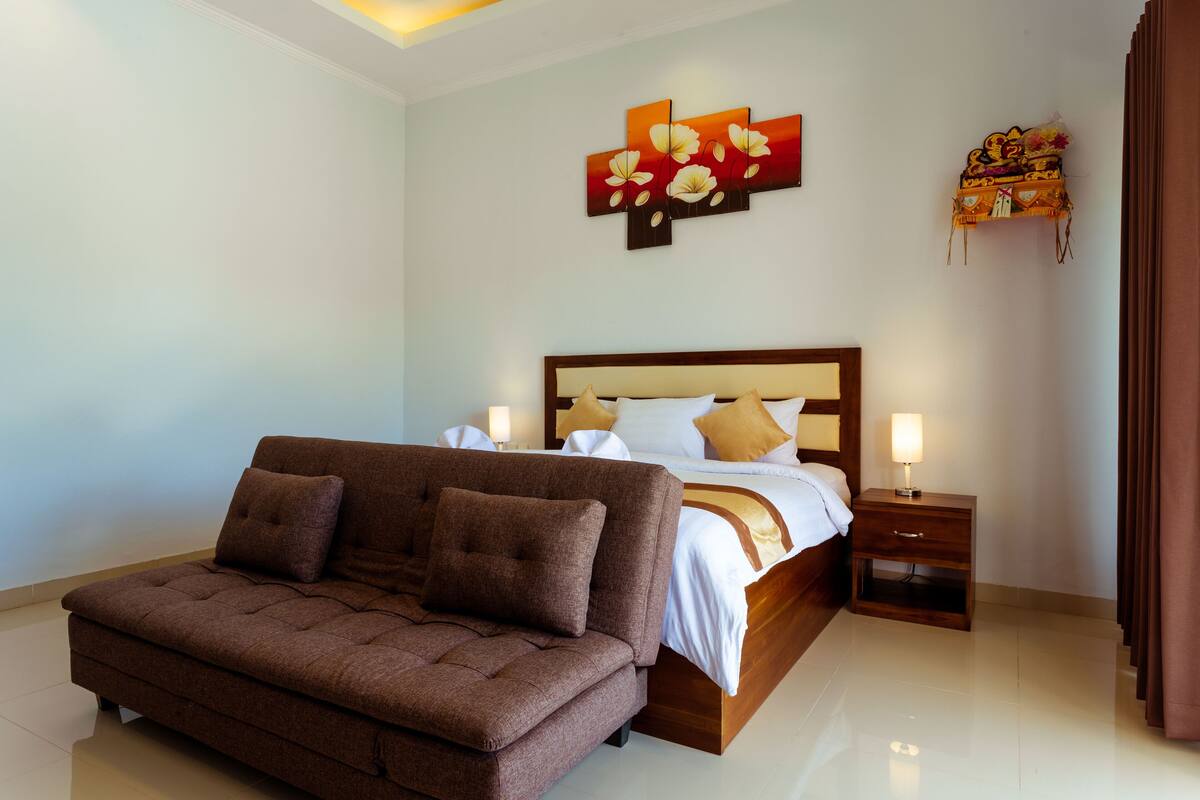 A modern bedroom with a large bed, a brown sofa, and a nightstand with a lamp.