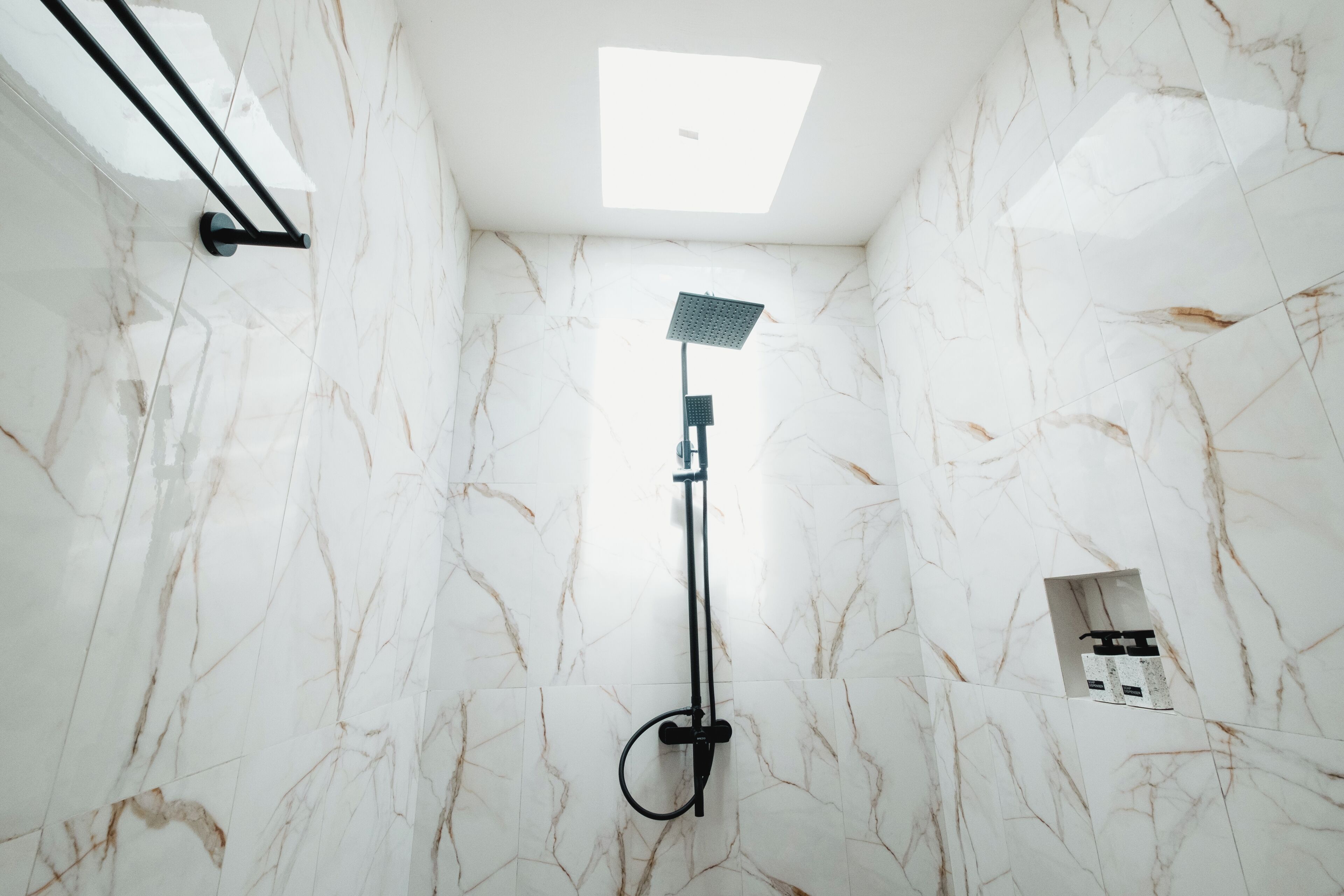 A bathroom with a shower, marble walls, and a ceiling light.
