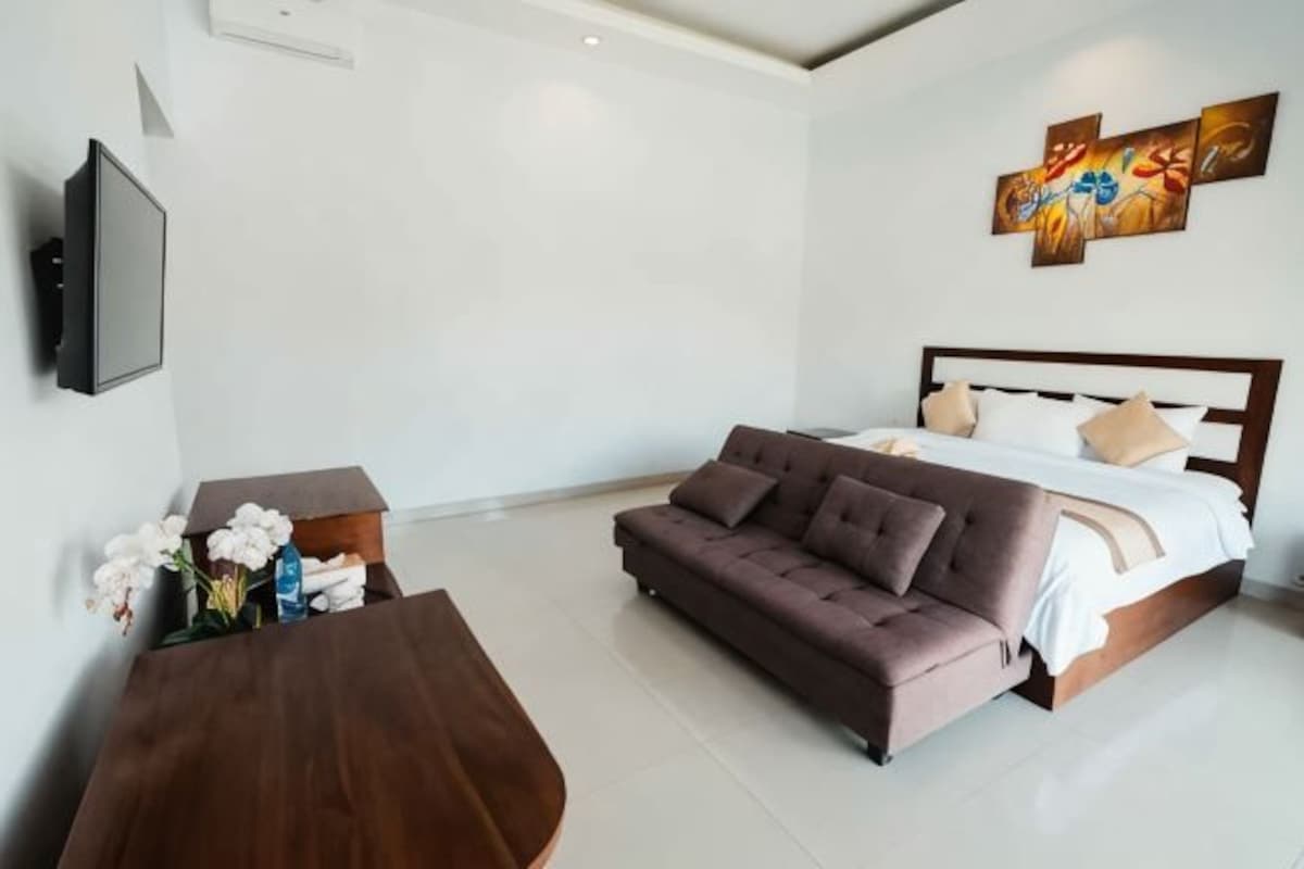 A modern bedroom with a bed, sofa, and a TV on the wall.