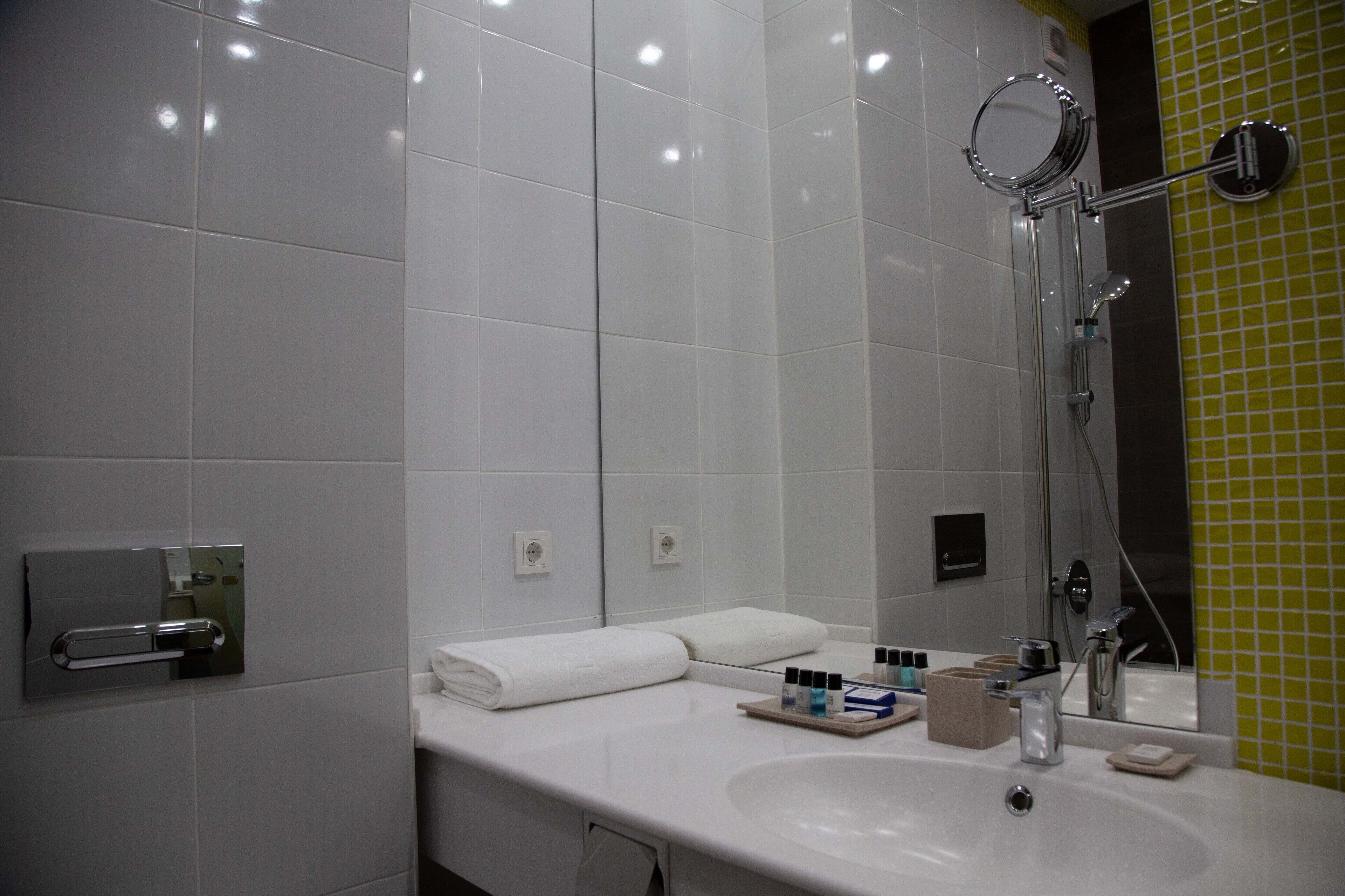 Un baño moderno con un lavamanos blanco, un espejo y una ducha con detalles cromados.