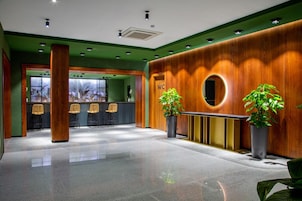 Vestíbulo de hotel con una mesa de recepción, un cartel de baño y dos plantas en macetas.