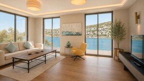 Un salon moderne avec un canapé, une table basse et un fauteuil jaune, de grandes fenêtres offrant une vue sur un plan d’eau et des bâtiments, et un tableau accroché au mur.