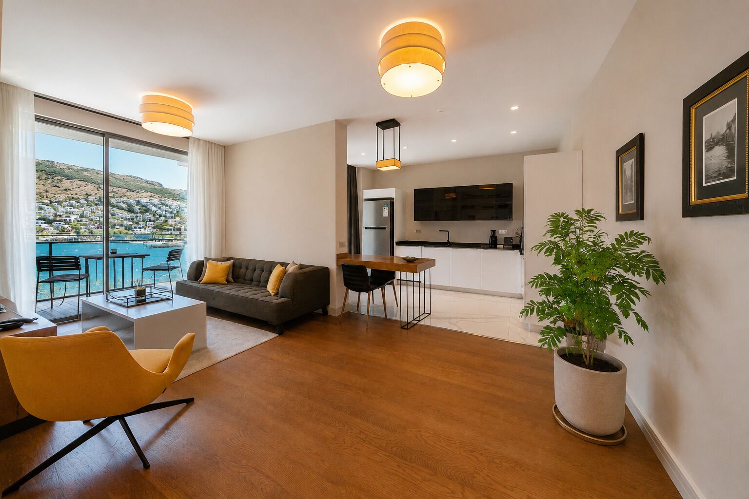 En moderne stue med sofa, gule lænestole, spisebord og et stort vindue med udsigt over et naturskønt landskab.