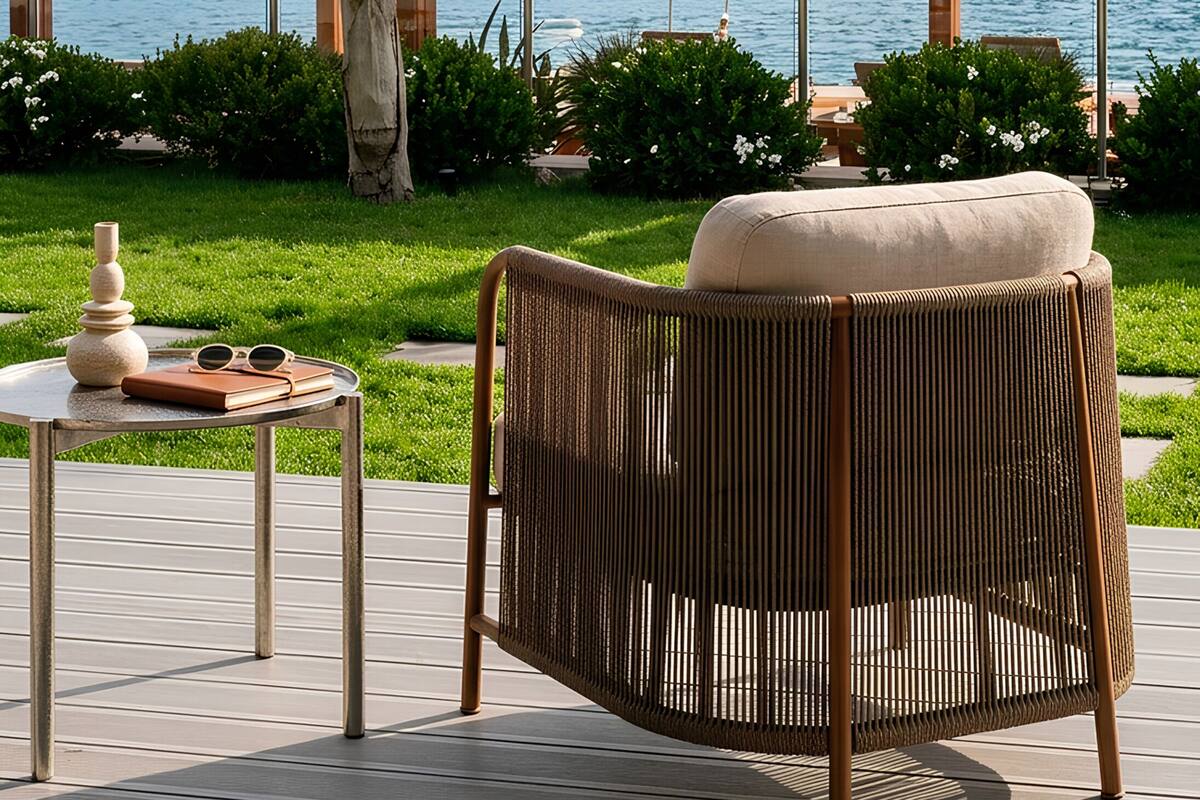 A patio with a wicker chair, a small table with a vase and sunglasses, and a pergola overlooking a marina with boats.