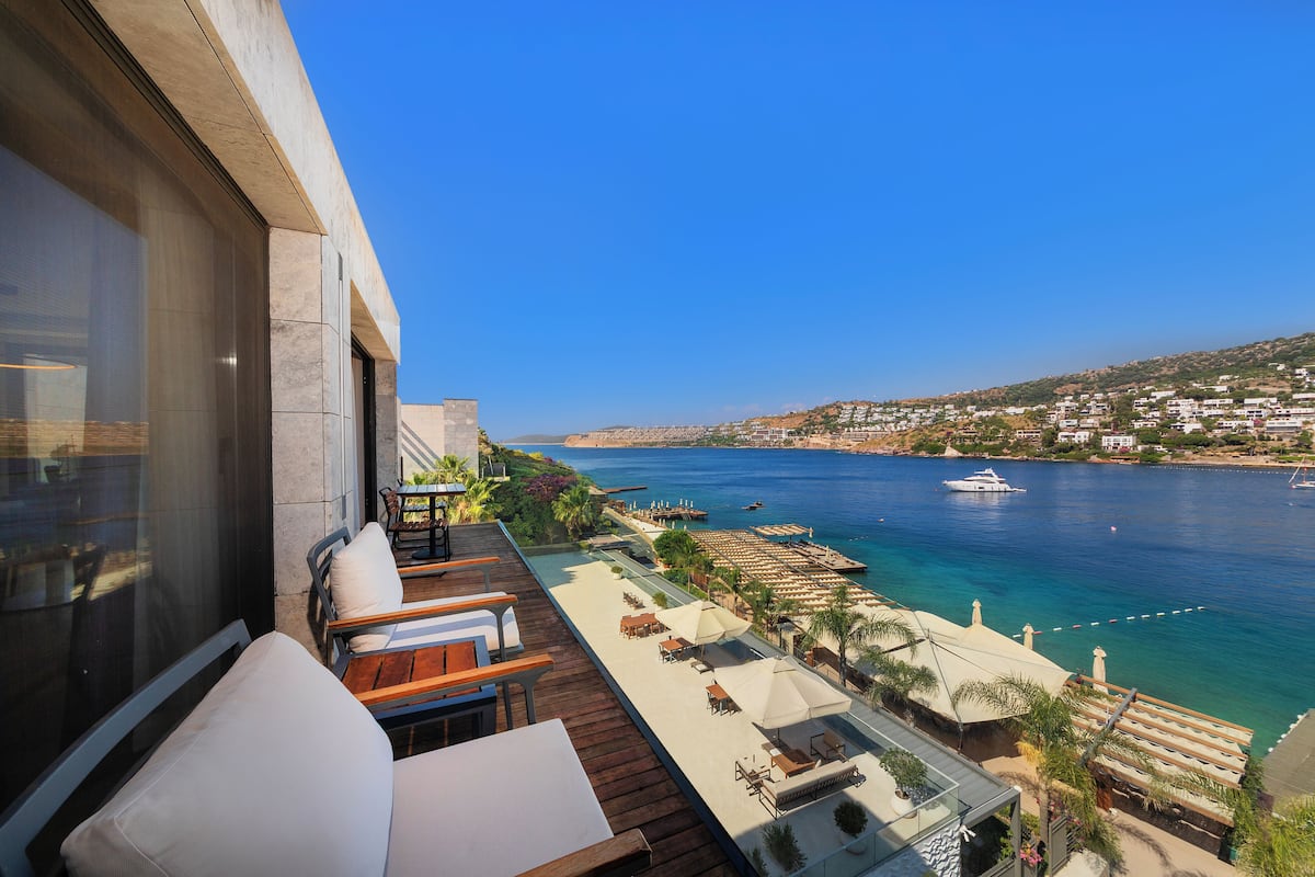 A balcony with outdoor seating, a view of the sea, and a boat in the distance.