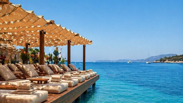 Une terrasse en bois avec des chaises longues et des parasols, donnant sur une eau d’un bleu limpide.