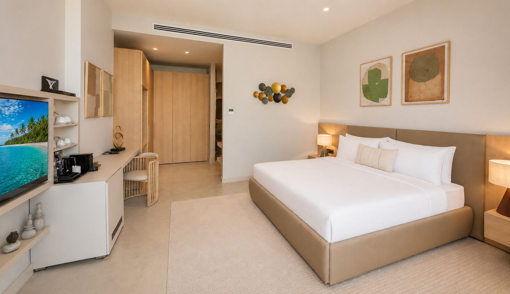A hotel room with a bed, bedside table, TV, desk, and a view of the beach.
