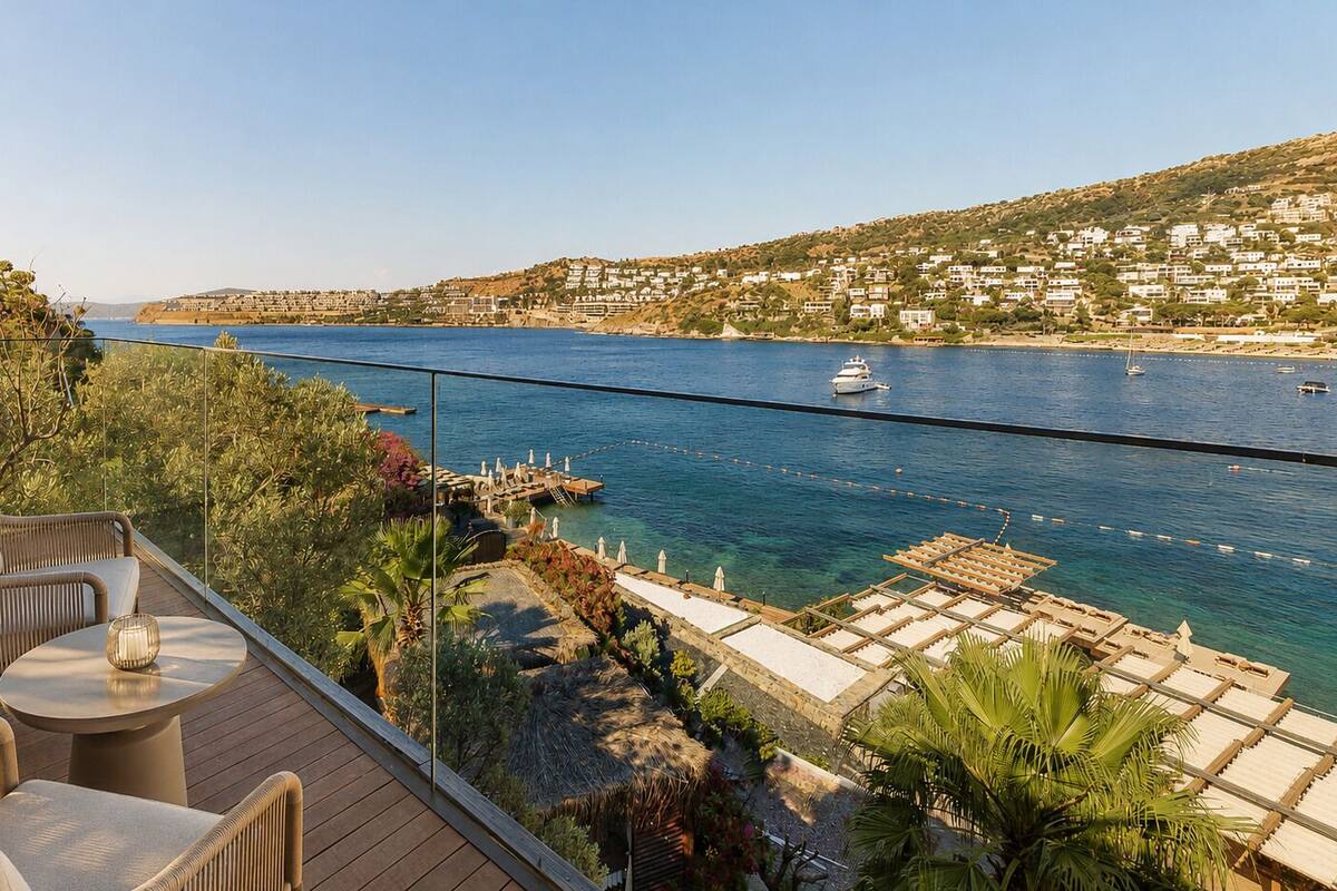 A balcony with outdoor furniture overlooking a coastal town and the sea.