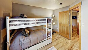 A bunk bed room with a wooden floor, a closet, and a door leading to another room.