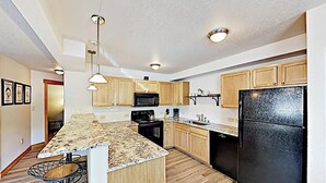 A modern kitchen with wooden cabinets, a granite countertop, a black refrigerator, and pendant lighting.