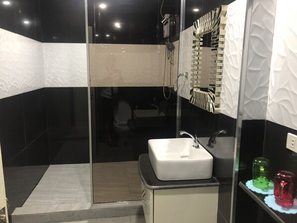 Un baño moderno con cabina de ducha de vidrio, un lavamanos blanco y un espejo con detalle decorativo en la pared.