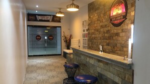 A bar area with a stone wall, two stools, a counter, and a neon sign. - Out Back (Olongapo)
