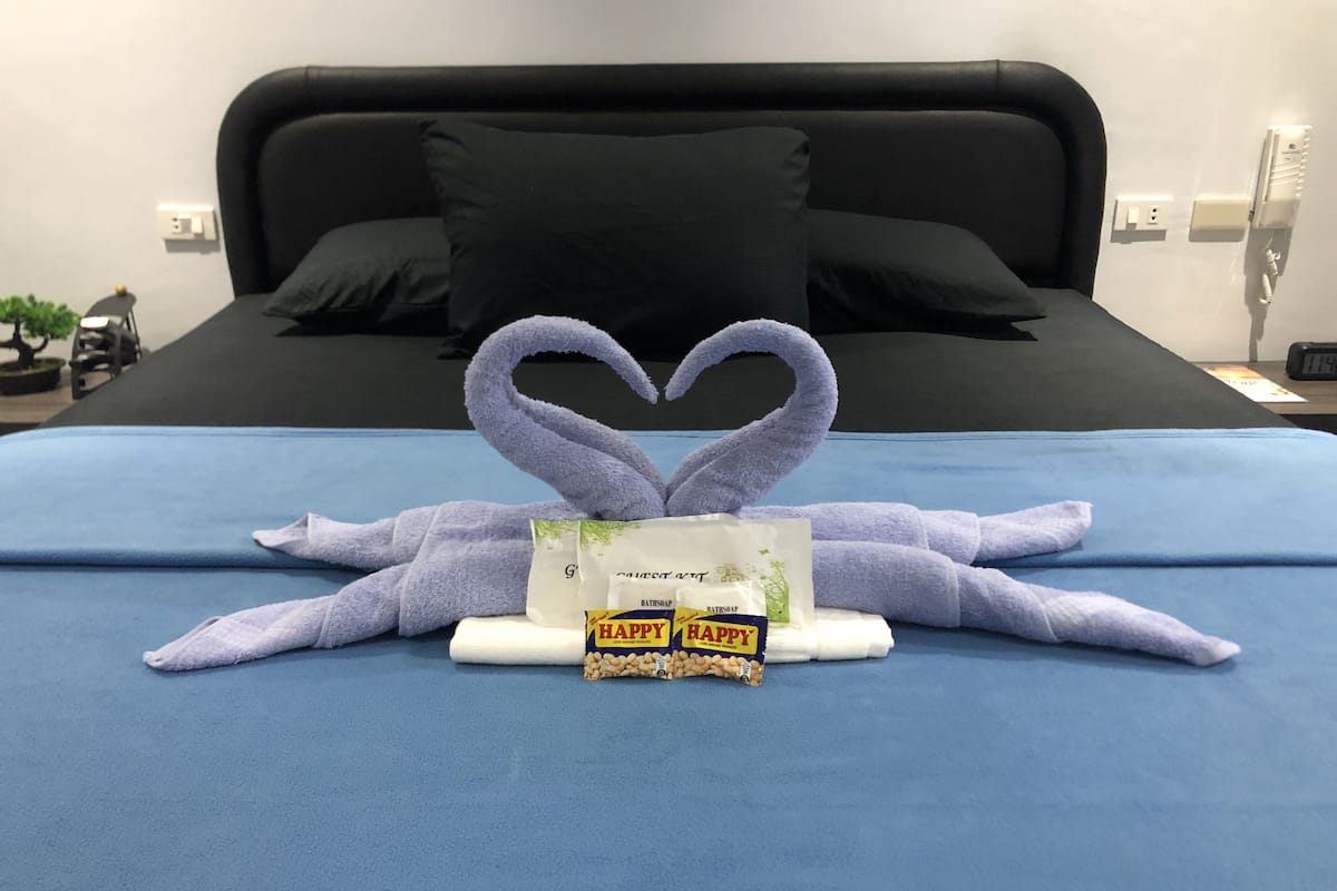 A neatly made bed with a heart-shaped towel arrangement and toiletries on a blue bedspread.
