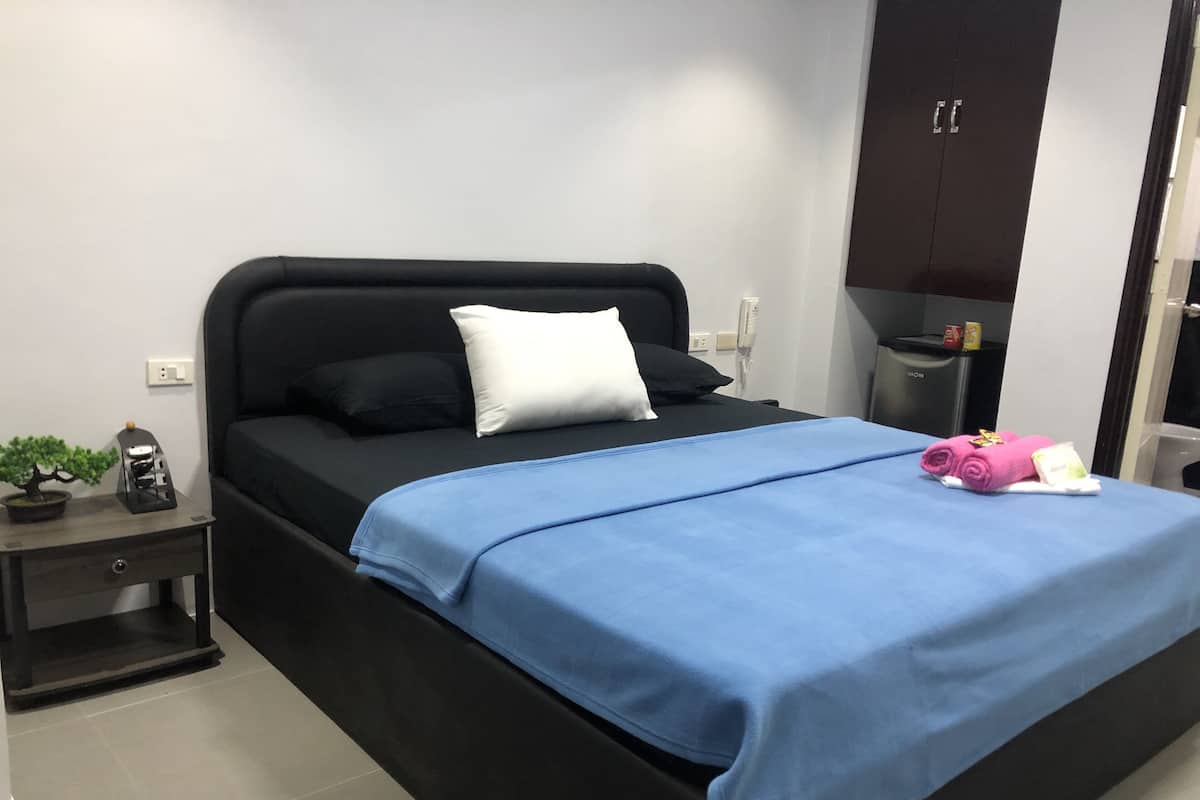 A modern bedroom with a black bed, a blue bedspread, and a nightstand with a plant and a phone.