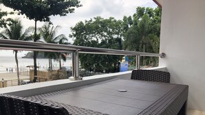 An outdoor dining area with wicker chairs and a table, overlooking a beach with palm trees and a swimming pool. - Out Back (Olongapo)