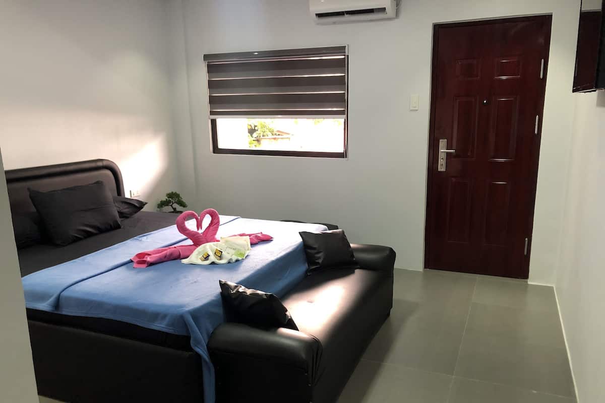 A bedroom with a bed, a window with blinds, a door, and a small potted plant.
