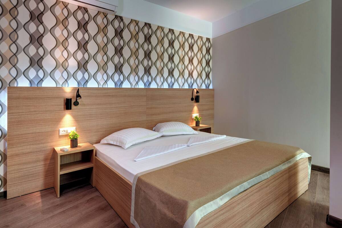 A neatly made bed with a wooden headboard, two bedside tables with lamps, and a patterned wall above.
