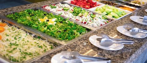 Un bufé con diversas opciones de comida, incluyendo ensaladas, frutas y verduras.