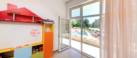 A children's play area with a whiteboard, colorful storage units, and a large sliding glass door leading to an outdoor pool area.