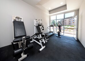 Un gimnasio con equipo de ejercicio, cinta de correr y vistas a una zona residencial a través de amplios ventanales.