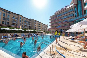 A swimming pool area with lounge chairs and umbrellas, surrounded by multi-story buildings with balconies.