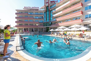 A hotel pool area with multiple levels of balconies, a clear pool, and sun loungers.