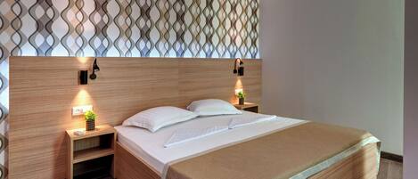 A neatly made bed with a wooden headboard, two bedside tables with lamps, and a patterned wall above.