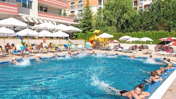 En swimmingpool där folk badar och solar, omgiven av parasoller och solstolar.