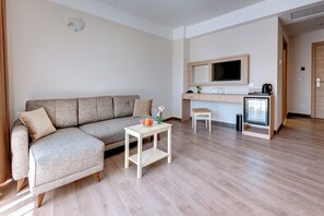 A modern living room with a sofa, a small table, a TV, and a kitchenette area. - Maria Palace (Nessebar)