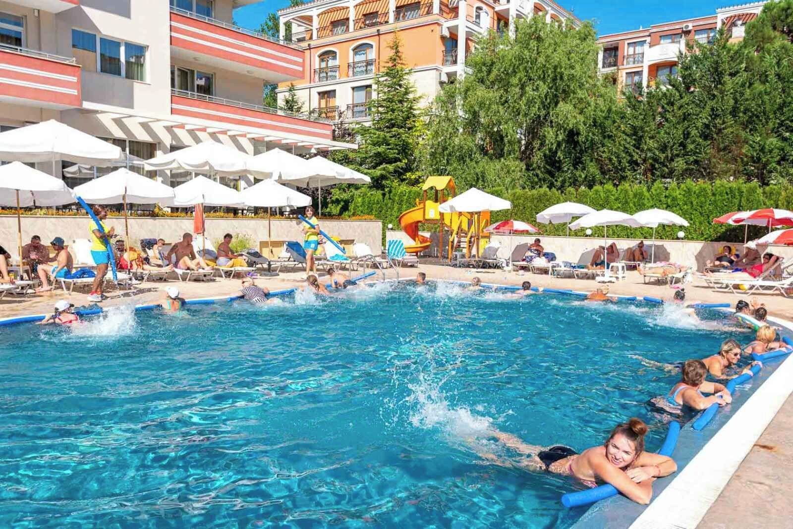 A swimming pool with people swimming and lounging, surrounded by umbrellas and lounge chairs.