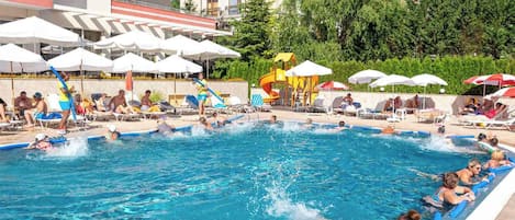 A swimming pool with people swimming and lounging, surrounded by umbrellas and lounge chairs.