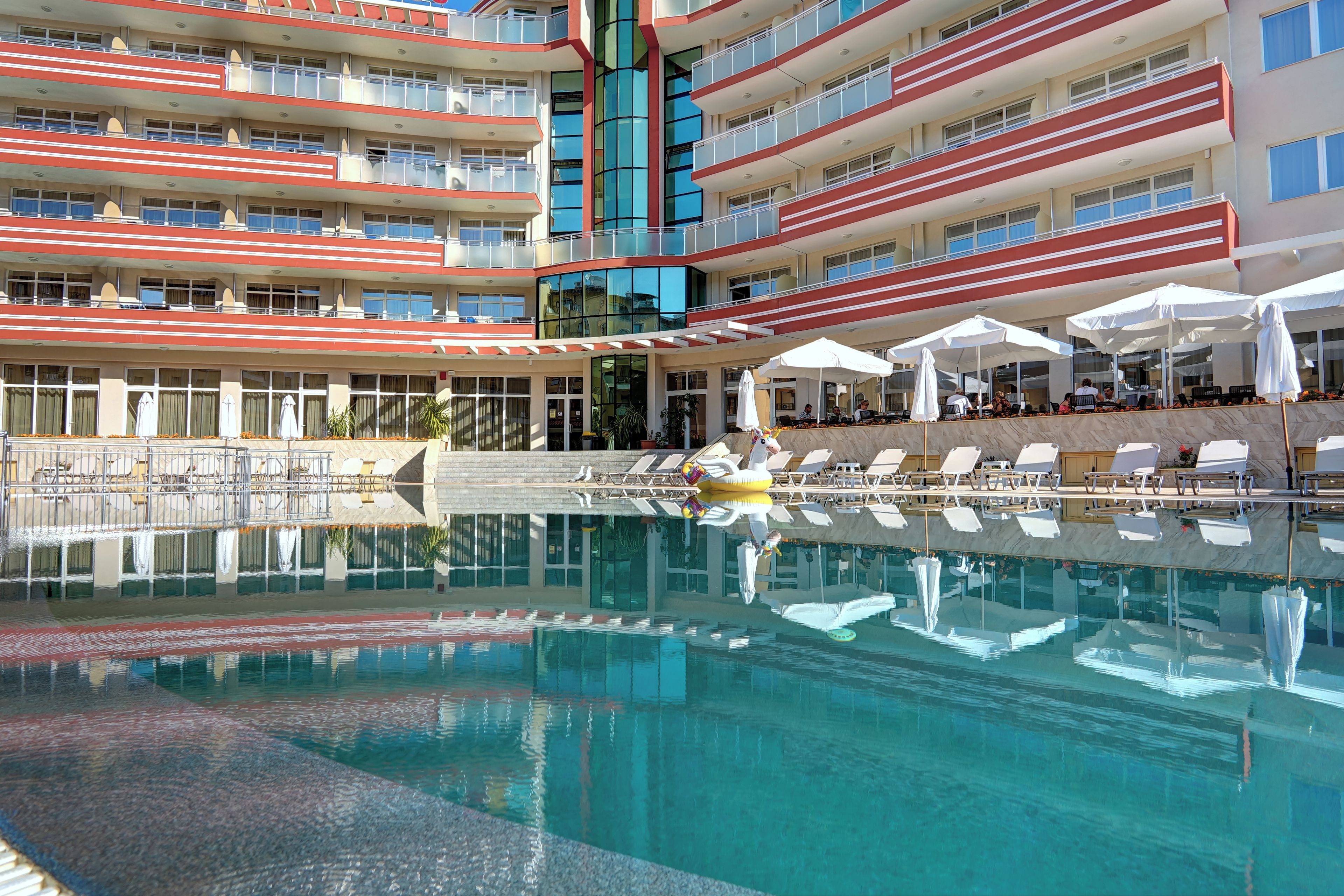 A multi-story hotel with a pool area, including sun loungers and umbrellas.