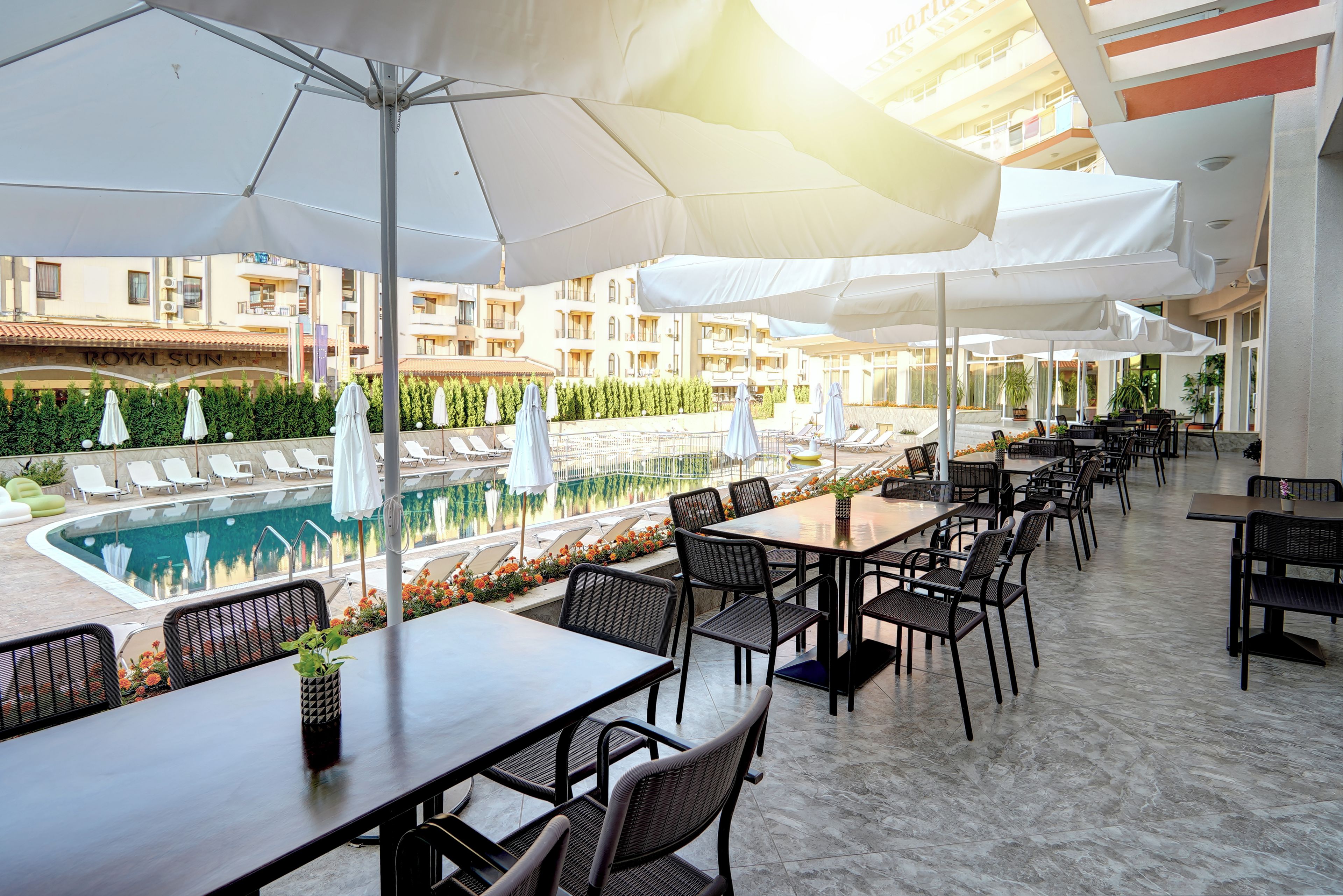 An outdoor dining area with tables and chairs, a pool, and umbrellas.