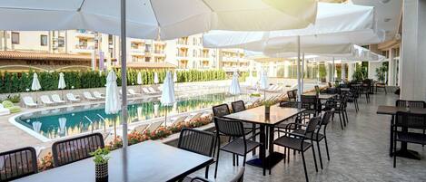 An outdoor dining area with tables and chairs, a pool, and umbrellas.