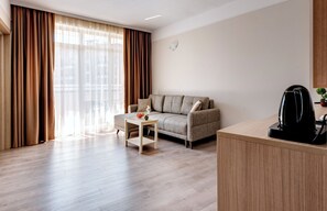 Un salon moderne avec un canapé, une petite table sur laquelle se trouve un panier de fruits, et une machine à café posée sur un comptoir en bois.