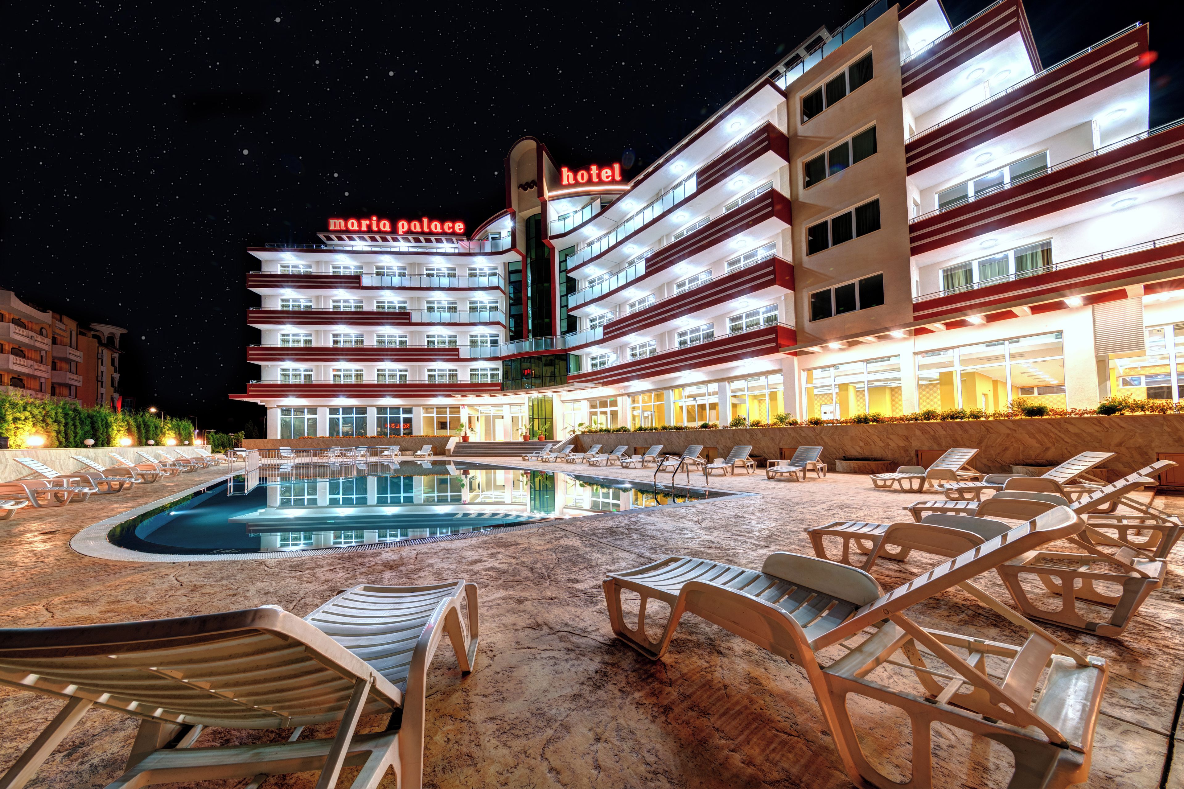 A hotel with a pool area, lounge chairs, and a night sky.