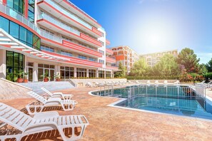 A swimming pool with lounge chairs, a building with balconies, and potted plants. - Maria Palace (Nessebar)