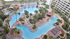 A large swimming pool with multiple lanes, surrounded by palm trees and lounge chairs.