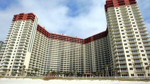 A high-rise hotel with a distinctive curved design, multiple balconies, and a beach view.