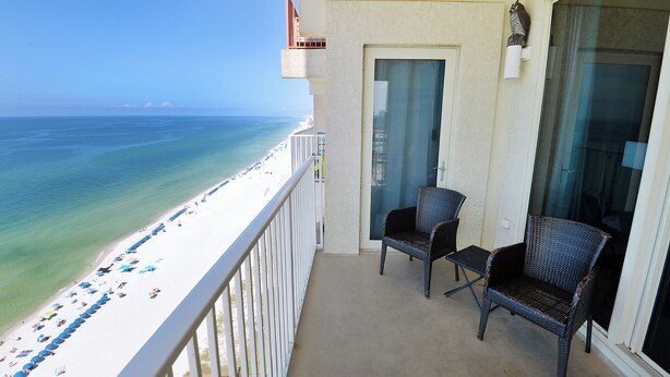 A balcony with two wicker chairs, a glass door, and a view of the beach and ocean.