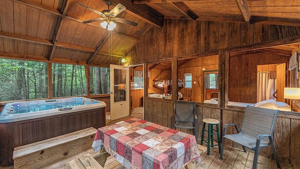 A rustic cabin with a wooden interior, a hot tub, a table with a quilt, and a view of the forest. - Romantic Get-away Cabin in the woods, w/Hottub next to coolest small town in USA (Victor)
