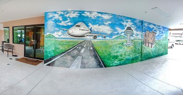 A mural of an airplane flying over a road with a lighthouse and buildings in the background.