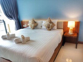 Habitación de hotel con una cama grande, dos almohadas, una mesita de noche con lámpara y toallas sobre la cama.